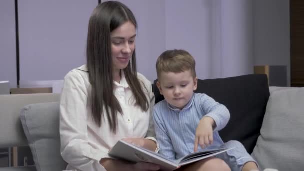 Mom and son are reading a book sitting on a sofa - Séquence, vidéo