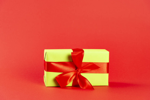 Christmas composition. Green gift box with a red ribbon on a red background. Side view. a Christmas gift - Foto, immagini