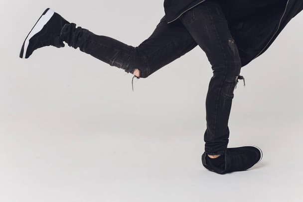 Close-up, Handsome young dancer dressed in black pants, a sweatshirt on a naked torso lifts one leg up while dancing street dance. - Photo, Image