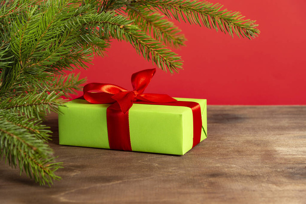 Christmas composition. Green gift box under the Christmas tree on a wooden table near a red background. a Christmas gift - Valokuva, kuva