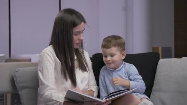Mom and son are reading a book sitting on a sofa - Metraje, vídeo