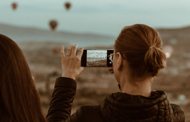 Woman taking a picture of a beautiful landscape with air balloons in Cappadocia, Turkey - Foto, afbeelding