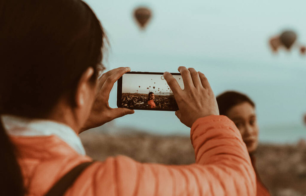 Woman taking a picture of a beautiful girlfriends with her smartphone against the Background of balloons in Cappadocia, Turkey - Fotoğraf, Görsel