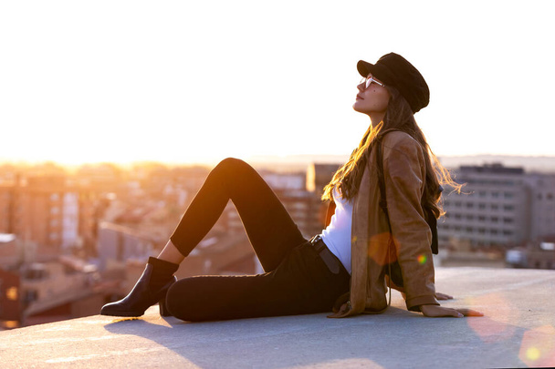 Pretty young woman enjoying time and sunset while sitting on the rooftop. - Zdjęcie, obraz