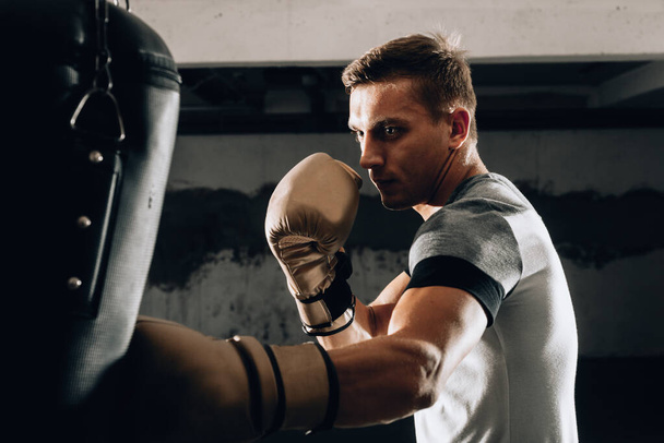Strong kickboxer man punching black sand bag on gym background - Photo, Image