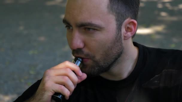 Handsome guy smoking an electronic cigarette outdoors. - Filmati, video