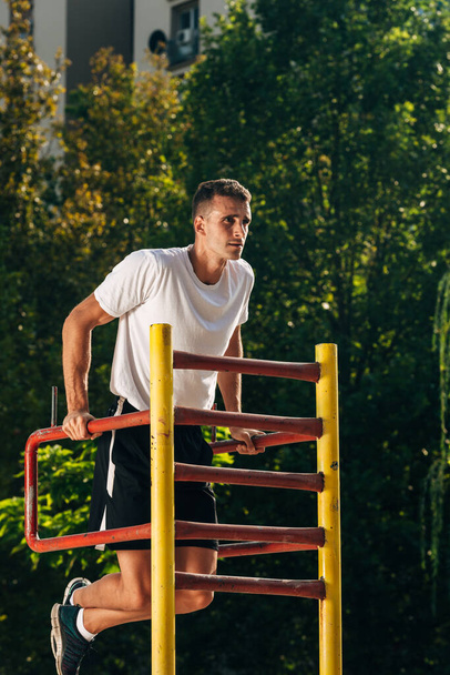 Muscular man doing dips in outdoor gym park during bright hot summer day - Foto, Imagem