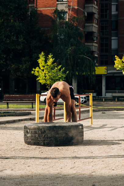Fit male athlete flipping a huge tire. Muscular young man doing crossfit exercise outdoors - 写真・画像