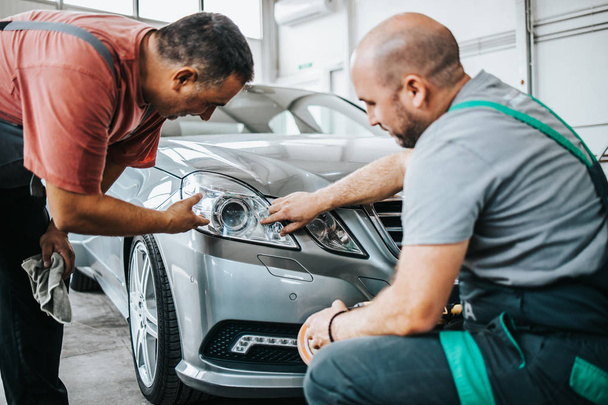 Two professional workers talking and checking car details during valeting and polishing procedure. - Zdjęcie, obraz