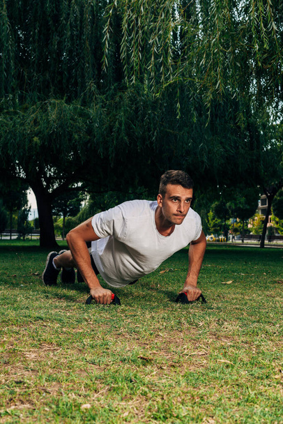 Trening koncepcja stylu życia.Muscular sportowiec ćwiczenia push up na zewnątrz w słonecznym parku. Bez koszulki męski model fitness w treningu crossfit na świeżym powietrzu - Zdjęcie, obraz