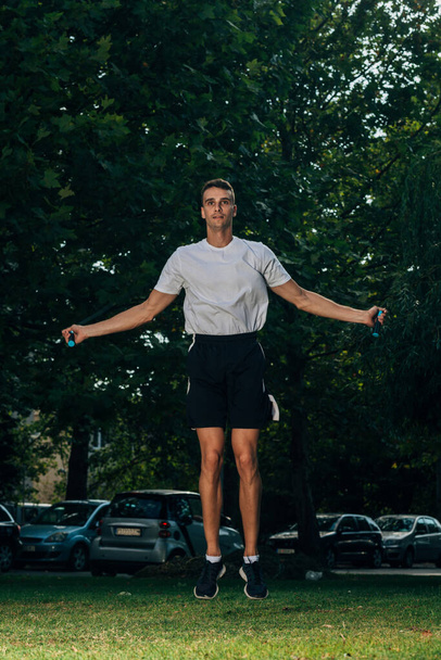 Handsome young man wearing sportswear and skipping rope at urban park - Fotografie, Obrázek