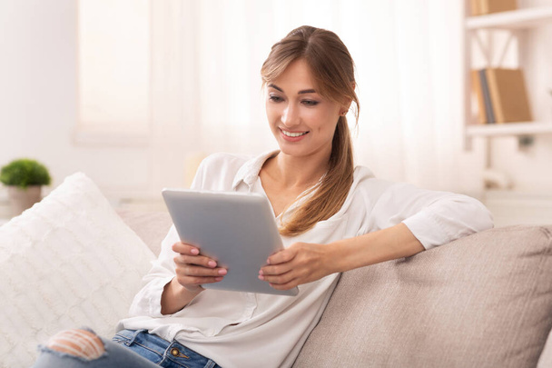 自宅でソファでリラックスしたデジタルタブレットを使用して笑顔の女性 - 写真・画像