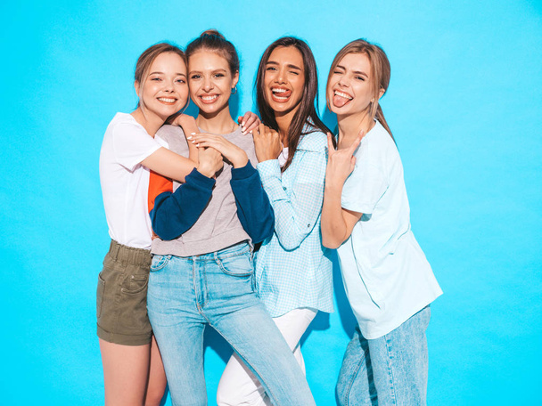 Three young beautiful smiling hipster girls in trendy summer clothes. Sexy carefree women posing near blue wall in studio. Positive models having fun and hugging.They show tongues - Photo, Image