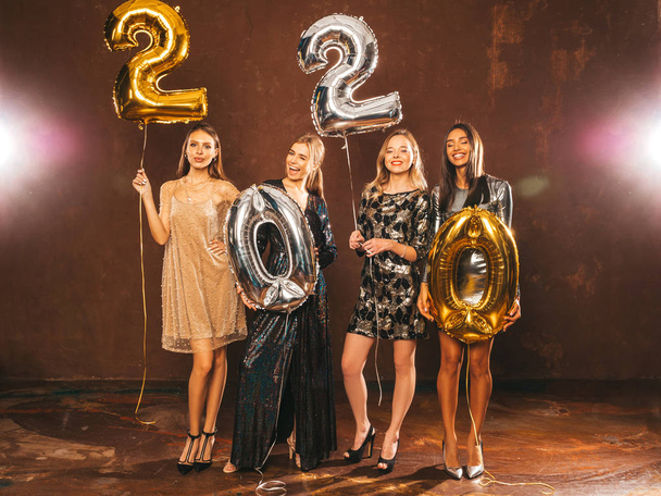 schöne Frauen, die Neujahr feiern. glücklich hinreißende Mädchen in stilvollen sexy Partykleidern mit goldenen und silbernen Luftballons 2020, die Spaß bei der Silvesterparty haben. Feiertag.Charmante Modelle  - Foto, Bild