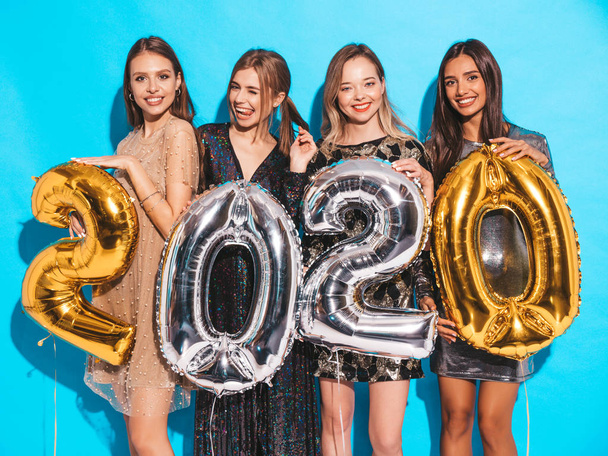 Beautiful Women Celebrating New Year. Happy Gorgeous Girls In Stylish Sexy Party Dresses Holding Gold and Silver 2020 Balloons, Having Fun At New Year's Eve Party. Holiday Celebration.Charming Models  - Valokuva, kuva