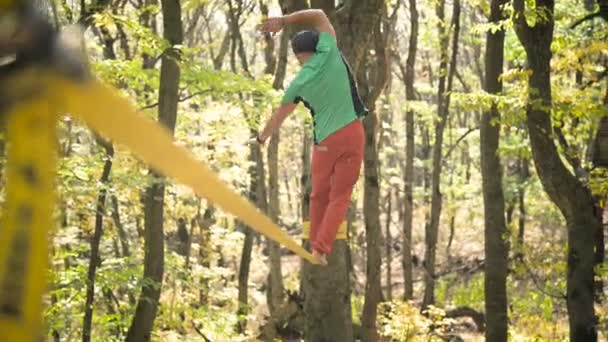 A Slack man aged with a beard in sportswear walks balancing on the slackline. The concept of sports activity at the age of 50 - Materiał filmowy, wideo