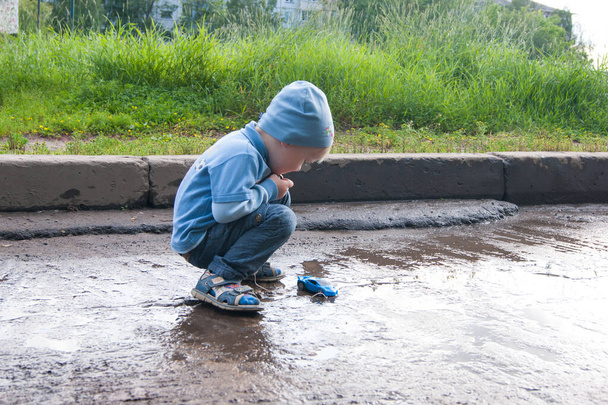 Üç yaşında, mavi şapkalı, kot pantolonlu, sandaletli, modası geçmiş bir uzaktan kumandalı arabayla serin bir yaz günü çalan beyaz bir çocuk.. - Fotoğraf, Görsel