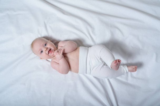 Mosolygó szőke baba feküdt a fehér lepedőn. Felülnézet - Fotó, kép