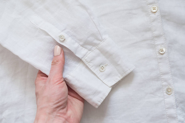 Sleeve of white shirt in female hand. Clothes concept. Details of clothes - 写真・画像