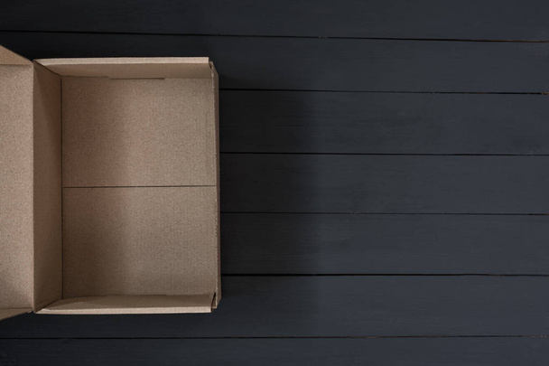 Пустой открытый картонный ящик на черном деревянном фоне. Концепция доставки. Вид сверху
 - Фото, изображение