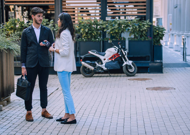 Vista frontal de una feliz pareja de ejecutivos caminando y hablando en la calle con un edificio de oficinas en el fondo - Foto, Imagen