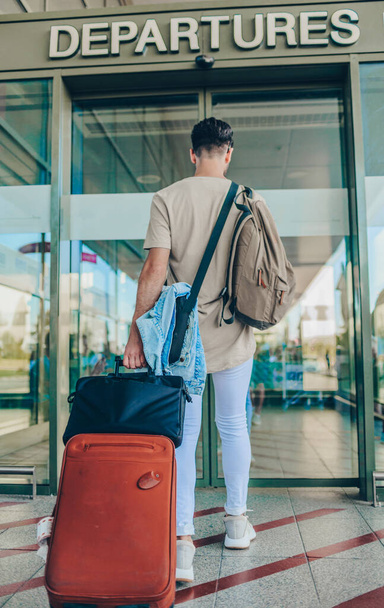Hombre con un bolso de mano en ropa casual sosteniendo su equipaje mientras está de pie en la sala del aeropuerto esperando su vuelo - Foto, imagen