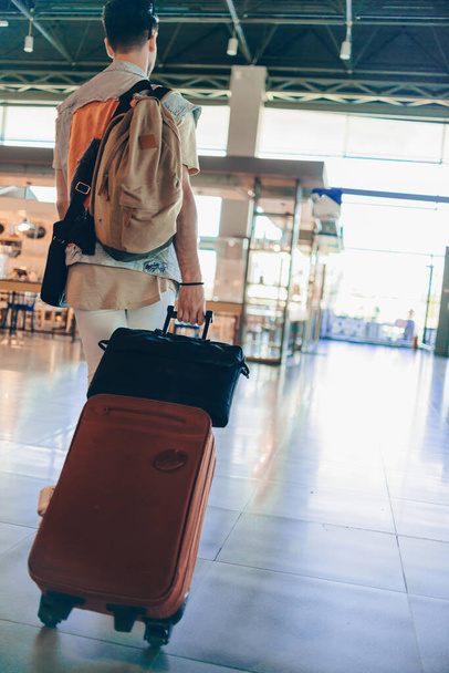 Tipo viajero con ropa elegante de estilo casual que se aleja con su equipaje mientras espera el transporte
 - Foto, Imagen