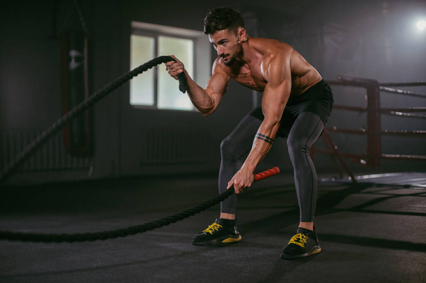 Hard exercises with ropes athletic man practicing cross fit training he make concentrated face while doing his workout - Foto, Imagem