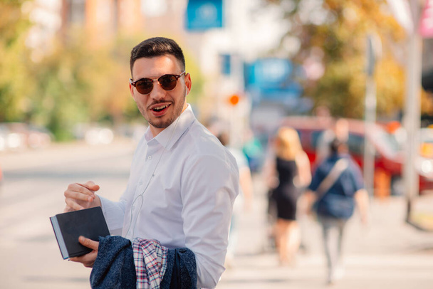 Jóképű üzletember a városban van, beszél, és a gyaloglás az utcán, notebook tartja a kezében. - Fotó, kép