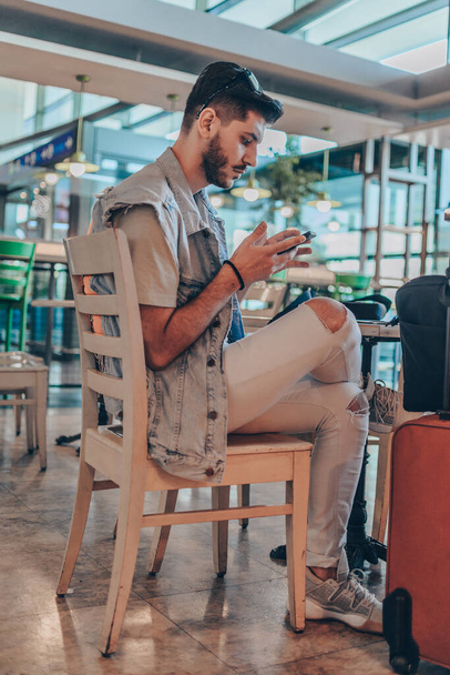 Havaalanı bekleme salonunda cep telefonuyla masada oturan düşünceli bir adam. - Fotoğraf, Görsel
