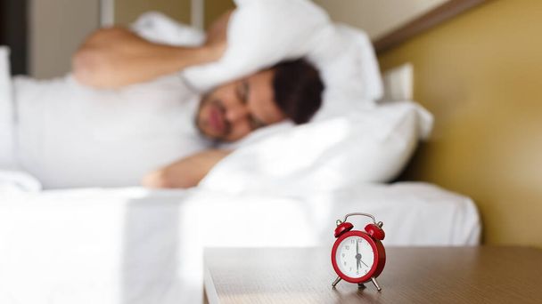 Hombre agotado siendo despertado por el despertador en su dormitorio
 - Foto, imagen