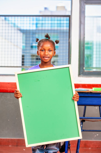 Afrikai lány általános iskolában, zöld táblával a kezében. - Fotó, kép