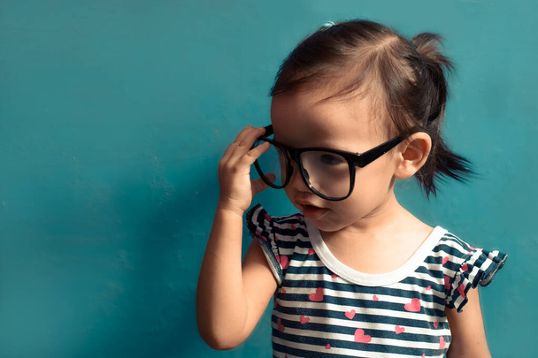 Beautiful serious children (kid, girl) holding glasses, blue isolated background with copy space. - Photo, Image