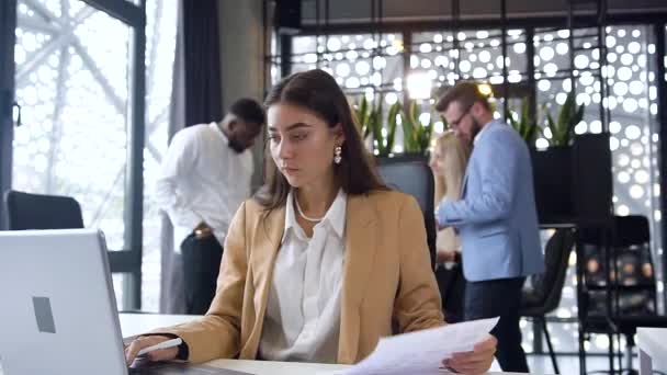 Close up of charming purposeful young businesswoman which entering datas from report to computer in modern office on office colleagues background - Πλάνα, βίντεο