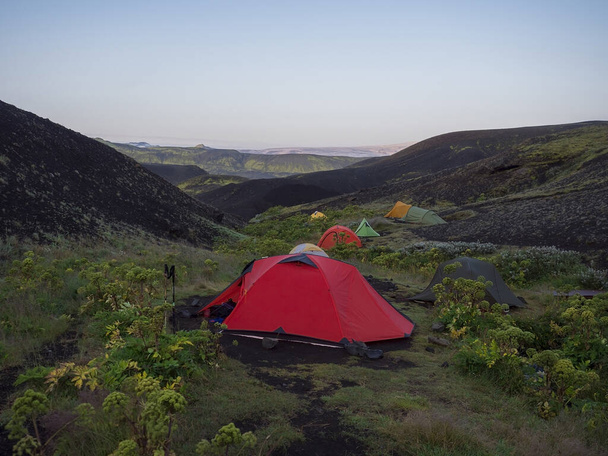 Tentes colorées au camping Botnar en Islande sur le sentier de randonnée de Laugavegur, vallée verdoyante dans un paysage volcanique au milieu des champs de lave avec vue sur le glacier Myrdalsjokull. Tôt le matin vue du lever du soleil
. - Photo, image