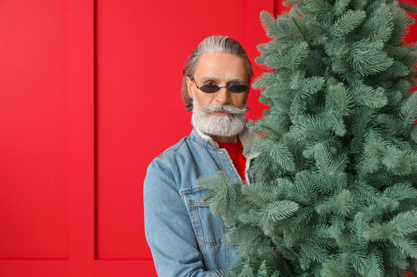 Portrait of stylish Santa Claus with Christmas tree on color background - Photo, Image