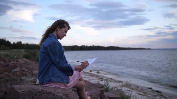 Genç bir sanatçı deniz kıyısında ilham arıyor. Bir kız 4k. Ağır çekim ile manzara resmi çiziyor. - Video, Çekim