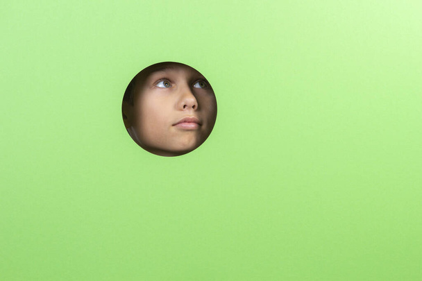 Kid watching through hole in green color background - 写真・画像