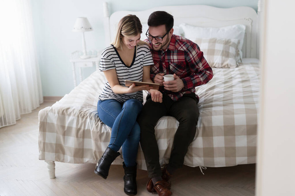 Happy young couple using digital tablet in bedroom - Фото, изображение