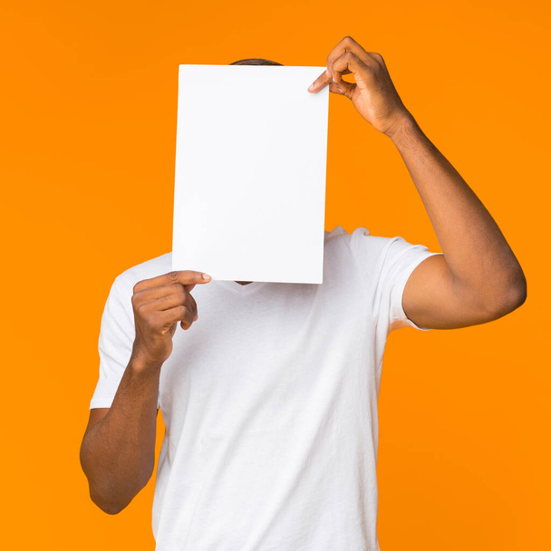 Black Man Covering Face With Paper Sheet Standing, Orange Background - 写真・画像