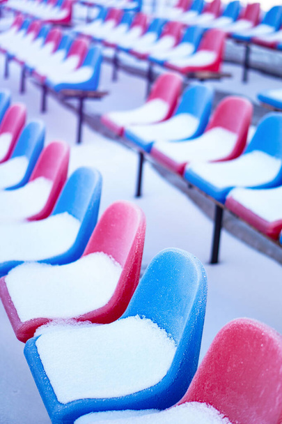 Sedili multicolori ricoperti di neve nello stadio in inverno. Le nevicate interferiscono con lo sport. Stadio non pulito. congelamento disastro ecologico
 - Foto, immagini