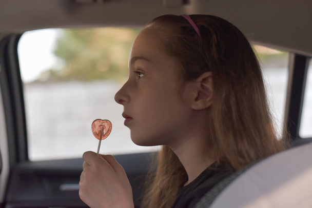 Little girl with a lollipop in his hand sitting in the car - Photo, Image