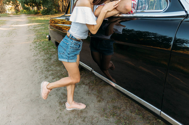 the girl approached the car in which the man is sitting, and leaned on the door of the car, flirting - Foto, Imagen