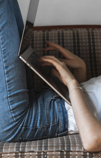 Woman with a laptop laying on a sofa. Study and work online, freelance. Self employed woman, girl working with her notebook laying on a couch with a phone, smartphone and ereader on table. - Foto, afbeelding