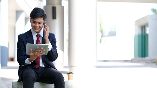 Joven hombre de negocios en traje negro hablando por móvil con partne
 - Foto, Imagen
