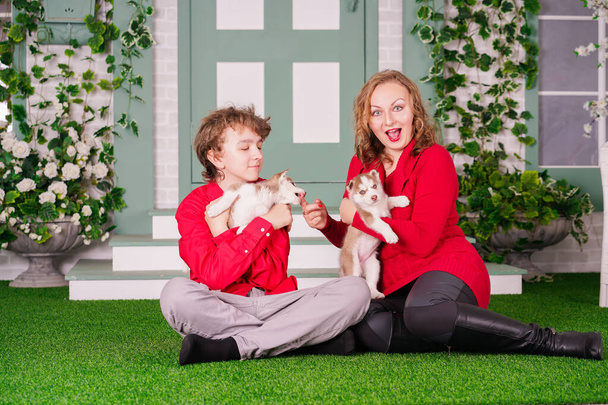 Счастливая мама и сын позируют на зеленой траве с двумя милыми щенками
 - Фото, изображение