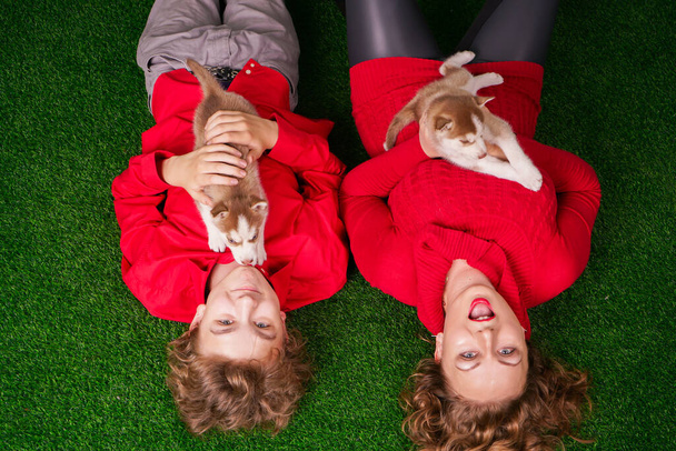 Bonne maman et son fils posent sur l'herbe verte avec deux petits chiots husky mignons
 - Photo, image