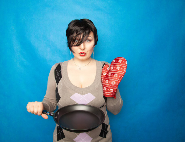 短い髪の女の子は大きな赤いキッチンの手袋と空のフライパンでセーターに立って調理する準備ができて - 写真・画像