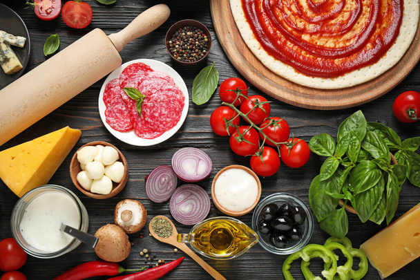Flat lay composition with pizza crust and ingredients on dark wooden table - Foto, Imagem