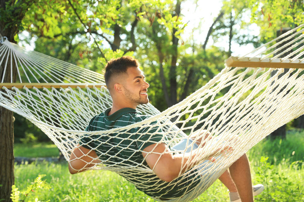 Молодой человек отдыхает в удобном гамаке в зеленом саду
 - Фото, изображение